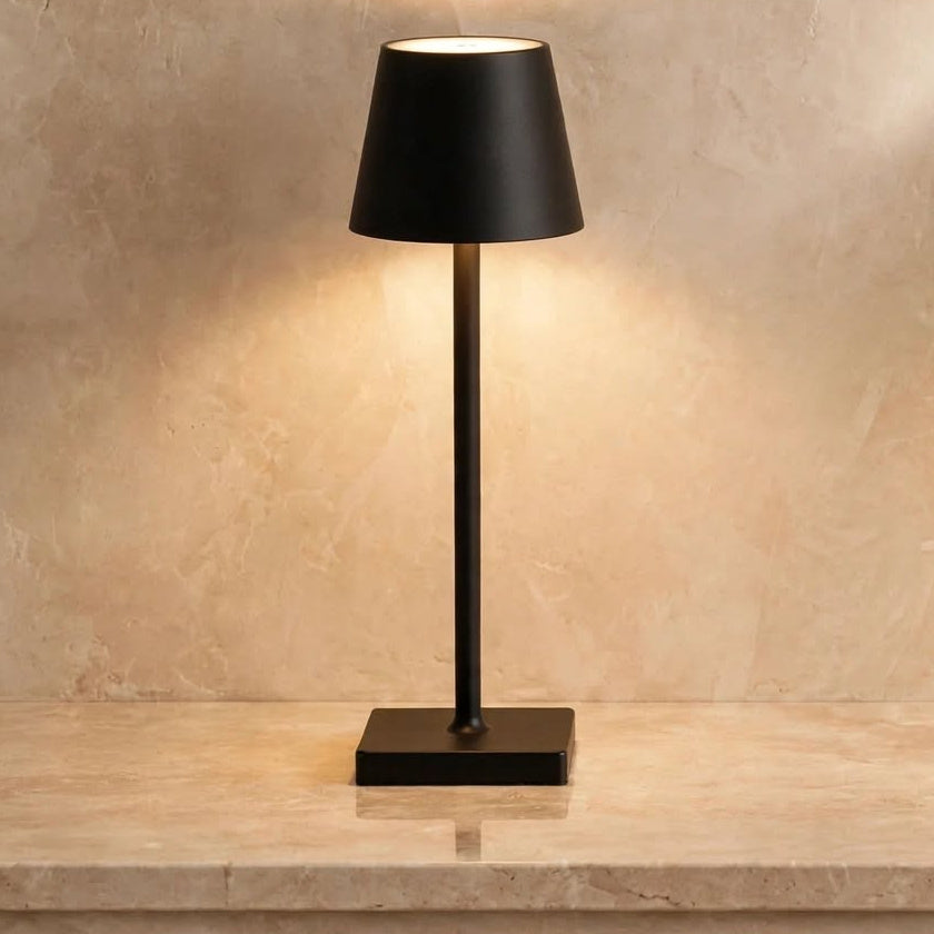 Lámpara LED portátil sin cables en color negro, encendida sobre una repisa de mármol